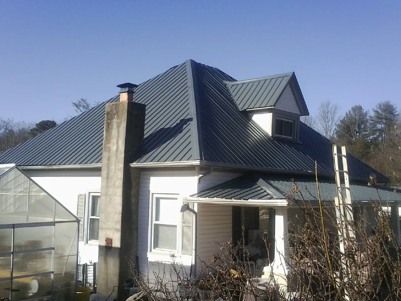Dark blue standing seam metal roof on a white farmhouse with dormer — Slate & Tile Roof Repair by Roofing Brothers in Beverly