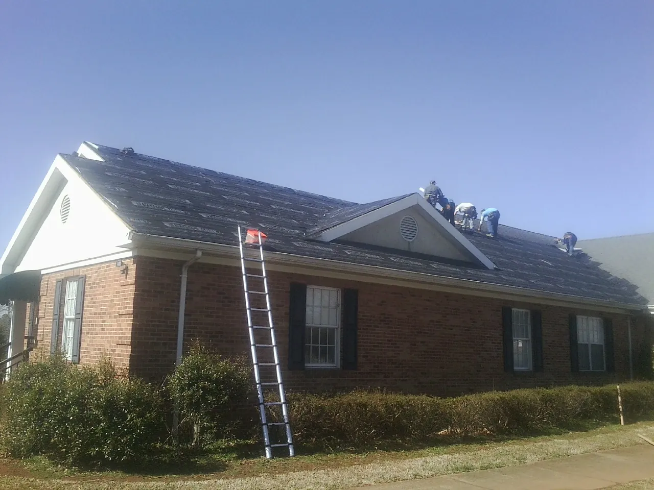 Crew tearing shingles off a brick ranch roof with a ladder set — Emergency Roof Repair work by our crew in Beverly