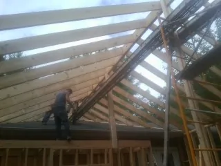 Rafters going up over a new addition with a worker on the wall in Beverly