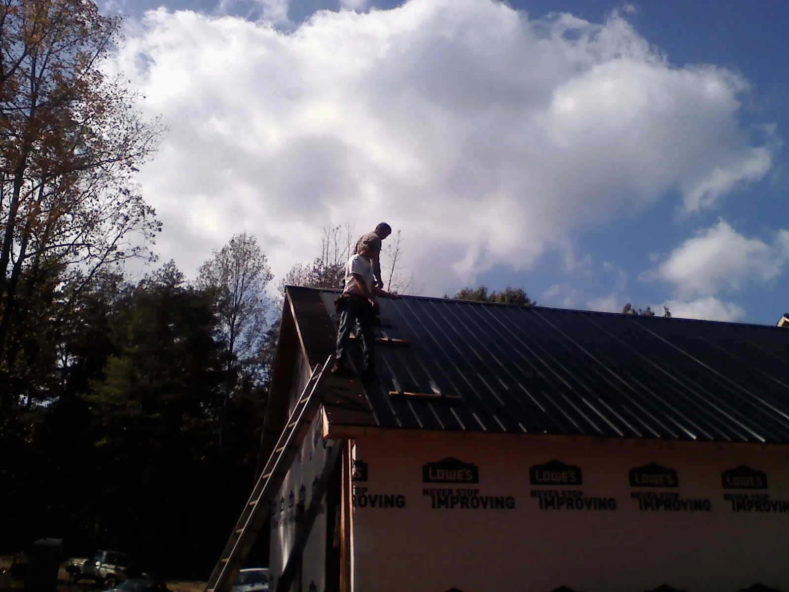 Roofer fastening dark metal panels high against a cloudy sky, from a Roof Inspection job in Beverly